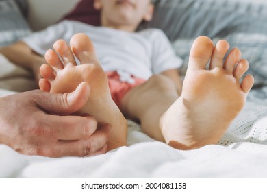 Dad tickles feet of kid. Boy lies on bed and plays with his father. Family, having fun at home
