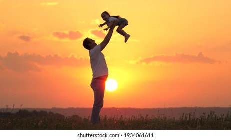 Dad Tosses His Happy Daughter Into Blue Sky At Sunset. Father And Healthy Child Play Together, Laugh And Hug. Carefree Kid Flies Into Sky. Child Is In The Arms Of Parent. Dad's Day Off. Happy Family