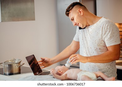 Dad Trying To Work, Cooking And Talk On Phone While Standing With His Newborn Babe In Home Office Interior