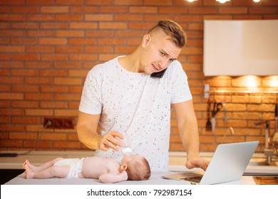 Dad Trying To Work, Cooking And Talk On Phone While Standing With His Newborn Babe In Home Office Interior