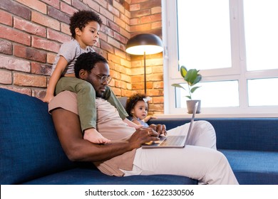 Dad with two children sitting in the living room on the sofa working on a laptop
