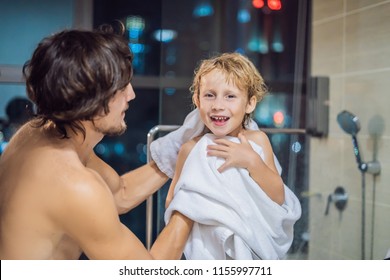 Dad wipes his son with a towel after a shower in the evening before going to sleep on the background of a window with a panoramic view of the city