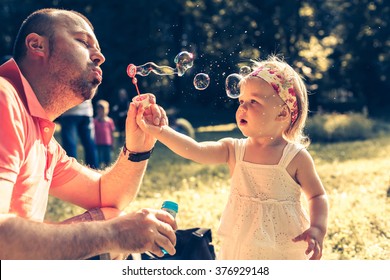 daddy and daughter blowing a bubbles in the park - Powered by Shutterstock