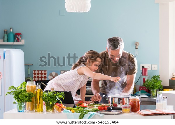 Daddy and his little daughter cooking bolognese\
sauce for spaghetti in the kitchen, there is steam escaping from\
the pan on cooking plate
