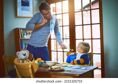 Daddy knows how to multitask. Cropped shot of a single father on a call while feeding his son at home.