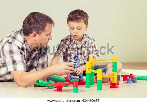 Daddy with little boy playing\
with toy  on the floor at the day time. Concept of friendly\
family.