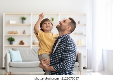 Daddy, look up. Excited little boy looking upwards with his father, child pointing with finger, man holding kid on hands, standing together at home - Powered by Shutterstock