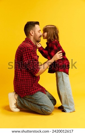 Daddy and Me. Kneeling father and child in matching outfits touching noses against vivid yellow background. Concept of International Day of Happiness, childhood and parenthood, Father's Day. Ad