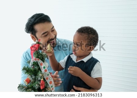 Daddy and son enjoy using times to decrorate christmas tree and take a selfie with mobile at home.