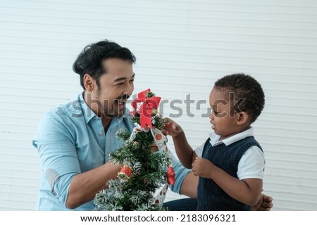 Daddy and son enjoy using times to decrorate christmas tree and take a selfie with mobile at home.