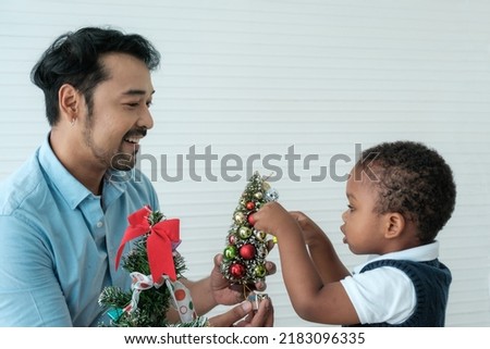Daddy and son enjoy using times to decrorate christmas tree and take a selfie with mobile at home.