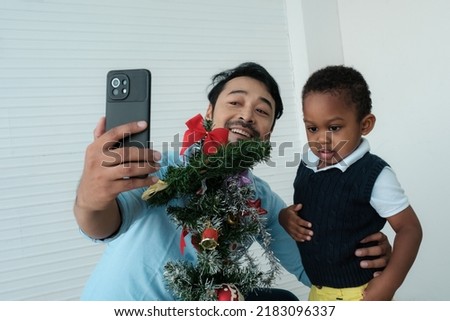 Daddy and son enjoy using times to decrorate christmas tree and take a selfie with mobile at home.