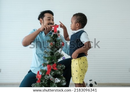 Daddy and son enjoy using times to decrorate christmas tree and take a selfie with mobile at home.