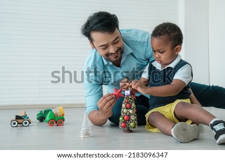 Daddy and son enjoy using times to decrorate christmas tree and take a selfie with mobile at home.