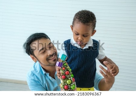 Daddy and son enjoy using times to decrorate christmas tree and take a selfie with mobile at home.