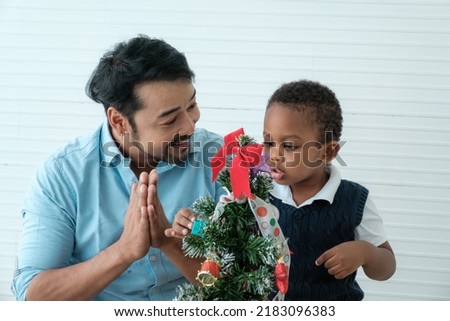 Daddy and son enjoy using times to decrorate christmas tree and take a selfie with mobile at home.