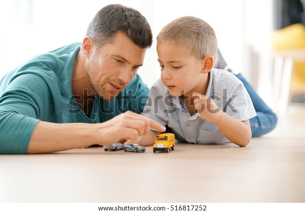 Daddy\
with son playing with car toys, laying on\
floor