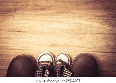 Daddy's boots and baby's sneakers, on wood background, fathers day concept.vintage color Daddy's boots and baby's sneakers, on wood background, fathers day concept.vintage color