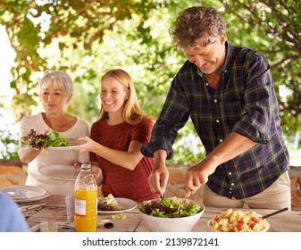 Dads in charge of dishing up. A view of a family preparing to eat lunch together outdoors.