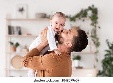 Dad's Love. Cute Young Father Kissing His Little Baby Daughter Cuddling And Bonding Holding Newborn Toddler In Arms Standing At Home. Parenting And Fatherhood Joy Concept