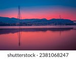 Daegu City sunset landscape at Gangjeong-Goryeong Weir or Dam with electricity pylons, power lines and mountains reflected on the Nakdong River, South Korea