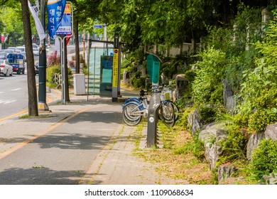 Daejeon, South Korea; June 8,2018: Three Rental Bicycles In Bike Rack In Front Of Bus Stop On Busy Street. 