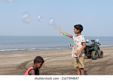 Dahanu, India - 25 December 2021, A Boy Playing With Water Bubbles At Dahanu Beach. Kids, Game, Sand, Childhood, Poverty, Child Labour, Sunny, Morning, Sea, India, Indian, Smile, Income, Livelihood.