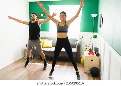 Daily Cardio Workout. Cheerful Young Woman Doing Jumping Jacks And Exercising With Her Boyfriend At Home