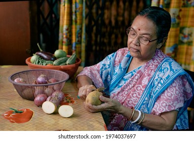 Daily life of an aged Bengali woman inside her home. She is seen chopping vegetables (mostly raw onions, potatoes etc.) with kitchen knife. Shot taken in Kolkata.