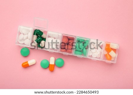 Daily pill box with medications and nutritional supplements on pink. Top view