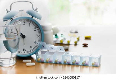 Daily Pill Box Of Vitamins And Medicines With Glass Of Water And Alarm Clock On The Table. Different Capsules And Tablets In A Plastik Dispenser. Healthy Lifestyle