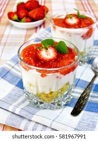 Dairy dessert with strawberries, corn flakes and yogurt in two glassful, spoon, blue napkin, berries in a bowl on linen tablecloth background