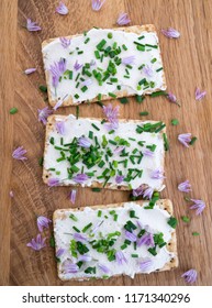 Dairy And Lactose-free Vegan Cream Cheese Spread Made From Cashew And Macadamia Nuts On Crackers With Fresh Chopped Chives And Edible Chive Flowers On A Wooden Chopping Board