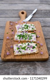 Dairy And Lactose-free Vegan Cream Cheese Spread Made From Cashew And Macadamia Nuts On Crackers With Knife, Fresh Chopped Chives And Edible Chive Flowers On Wooden Board With Shallow Depth Of Field