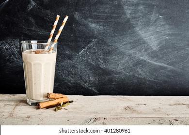 Dairy smoothie with two swirl colored straws and a sprinkle of cinnamon in a large glass on a long table