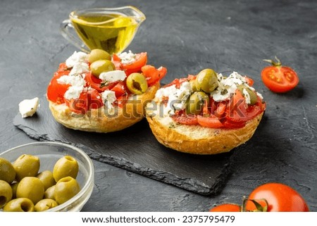 Dakos, Cretan dish with bread, tomatoes, butter, herbs and feta cheese or cottage cheese on a dark background.