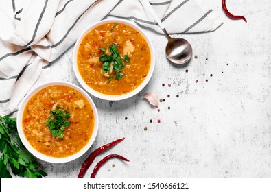 Dal - Traditional spicy Indian soup of red lentils and vegetables in a white bowl and spices on a grey background, top view. Indian and vegetarian food.