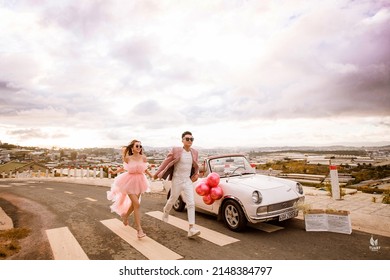 Dalat City, Vietnam - November 2021: Rich Asian Couple Wearing Sunglasses Posing Next To A White Car. Man's Hand Holding A Bunch Of Balloons.