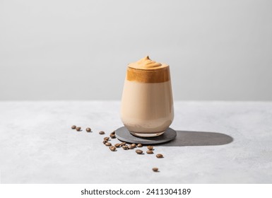 Dalgona coffee. Whipped instant coffee in a glass with beans and shadow on a light background.  The concept of a trendy and popular drink. Free space for text. - Powered by Shutterstock