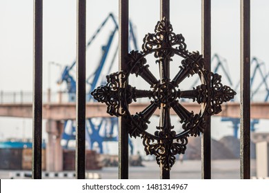 Dalian, Liaoning, China - May 21 2009: A decorated wrought iron fence at the harbour, behing the crane booms in Dalian Harbour