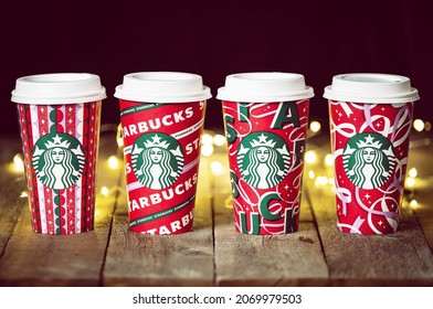 Dallas, Texas - November 5, 2021: A row of Starbucks coffee in the new 2021 designed holiday cups. Displayed on wooden rustic table and festive Christmas string lights in the background.