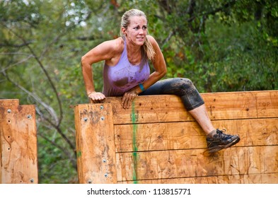 DALLAS, TEXAS - SEPTEMBER 15: Unidentified Female Participant Climbs Over A Wooden Wall Obstacle In The Dash Of The Titans Mud Run Race On September 15, 2012 In Dallas, Texas.