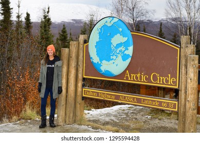 Dalton Highway, Alaska, United States - October 13, 2013: Female Tourist Standing By The Sign Board For The Arctic Circle Along The Dalton Highway In Alaska With Model Release