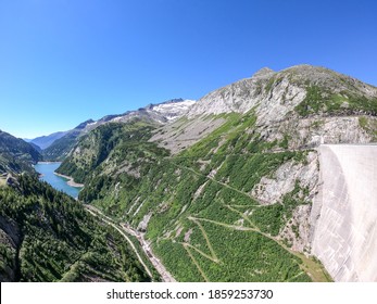 A Kölnbreinsperre dam in Austria. The dam is build in high Alps. The lake stretches over a vast territory. The dam is surrounded by mountains. In the back there is a glacier. Controlling the nature