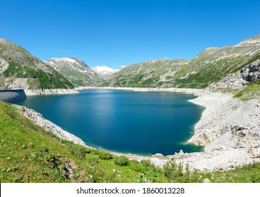 A Kölnbreinsperre dam in Austria. The dam is build in high Alps. The lake stretches over a vast territory. The dam is surrounded by mountains. In the back there is a glacier. Controlling the nature