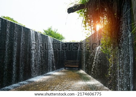 Dam is the flowing water like a small waterfall curtain. Water overflowing the mortar weir during the rainy season with bench is under and sunlight at Pang Sawan Weir, Uthai Thani, Thailand.