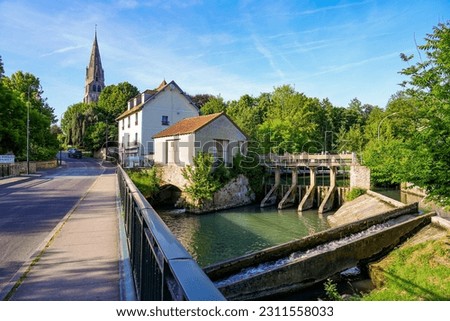 Dam on the Grand Morin river next to a tannery containing a watermill, bypassed by a concrete fish ladder, in front of the Church of Saint Denys and Saint Foy in Coulommiers, Seine et Marne, France