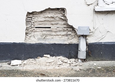 A damaged area on an external house wall with exposed plaster and wood