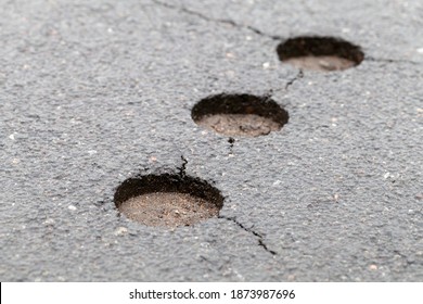 Damaged asphalt road with cracks and pavement test holes, close-up photo