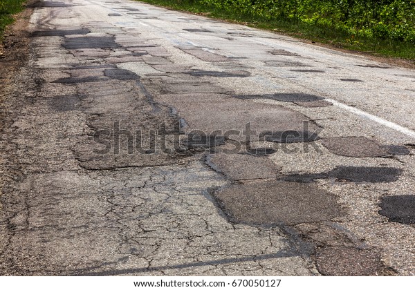 Damaged asphalt road
with potholes. Bad road. Repair. Patch repair of asphalt. Bad
asphalt, dangerous road, Broken automobile road, cracks, holes,
potholes in asphalt
